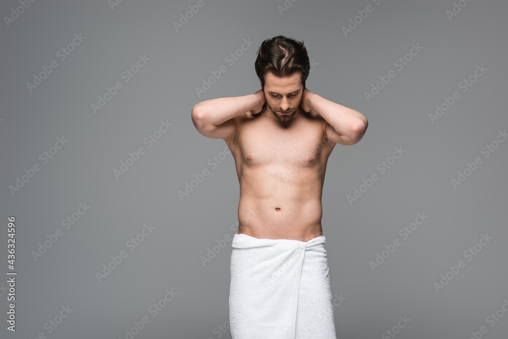 muscular man wrapped in towel standing and looking down isolated on grey.