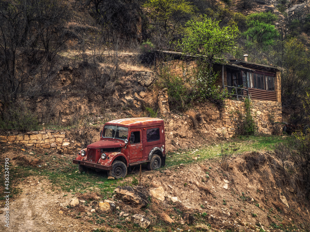 Rusty Gaz-69 car on a slope near a house in a mountain village. Dagestan.