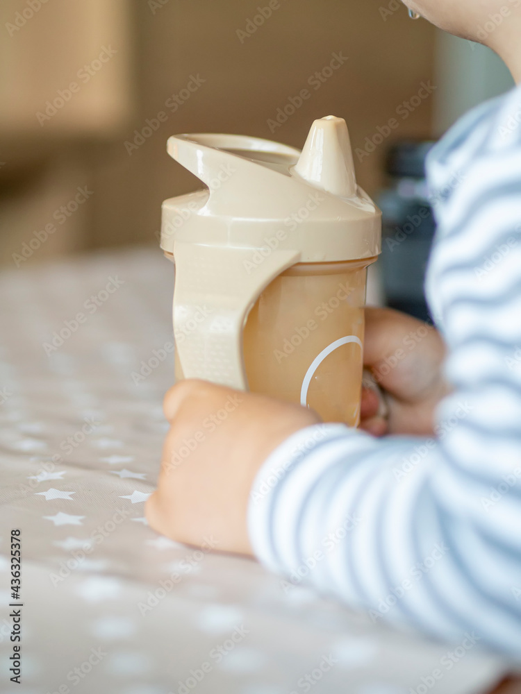 baby holding a bottle with handles to learn how to drink water. Water bottle for babies. Focus on the bottle and baby hands using it. baby holding a bottle with handles to learn how to drink water. Water bottle for babies. Focus on the bottle and baby hands using it.