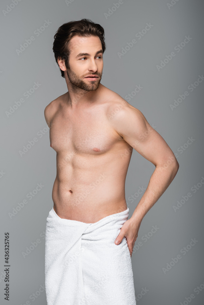 young muscular man wrapped in white towel looking away isolated on grey.