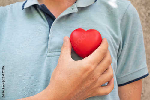 hand holding a red heart to his chest.Health, medicine, cardiology concept.Heart health insurance, organ donation concept.World mental health day.World heart health day.heart selective focus.