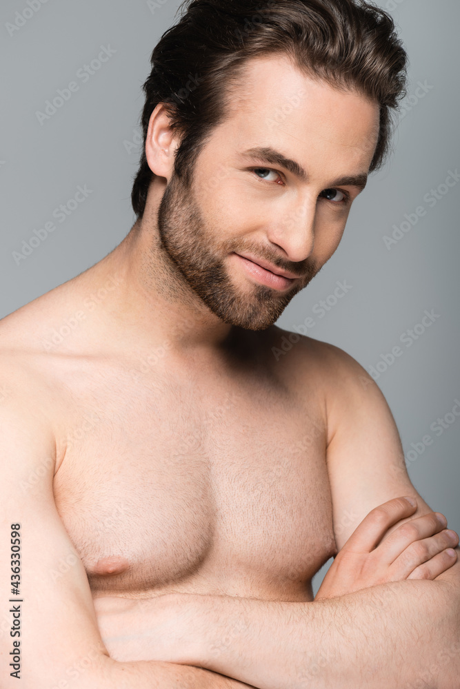 joyful and muscular man posing with crossed arms isolated on grey.