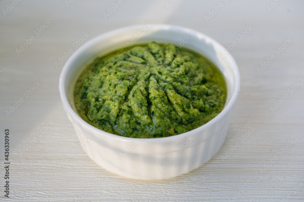Homemade ramson green pesto sauce in white ceramic saucer over gray textured background . Top side view with copy space. Horizontal image Homemade ramson green pesto sauce in white ceramic saucer over gray textured background . Top side view with copy space. Horizontal image