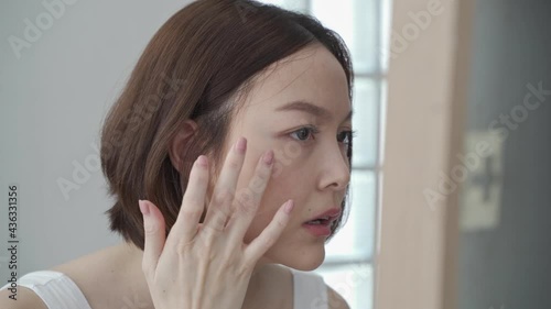 attractive beautiful short hair asian woman worry looking into mirror for face skin care condition. Frustrated Young female Examining Her Face While Looking At The Mirror in bathroom. annoy facial age