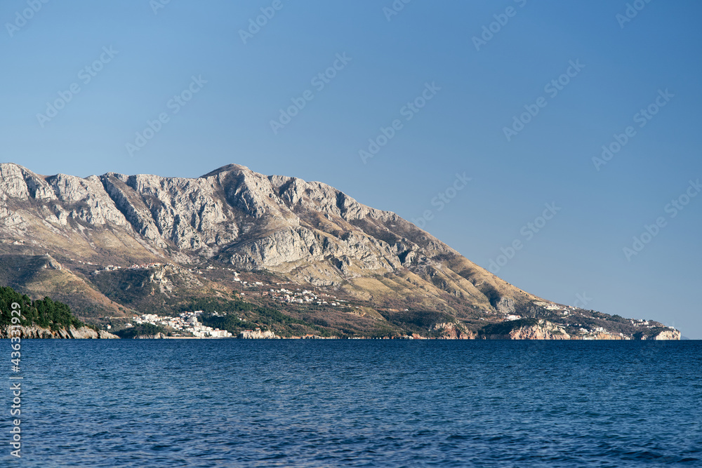 Panorama of mountains with green trees by the sea against the background of a bright blue sky