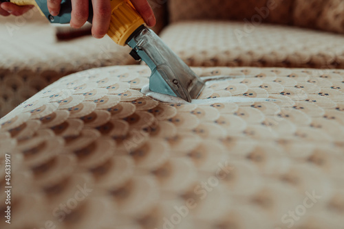 Close-up of housekeeper holding modern washing vacuum cleaner and cleaning dirty sofa with professionally detergent. Professional springclean at home concept photo