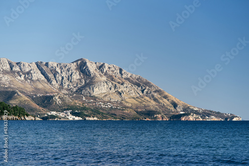 Panorama of mountains with green trees by the sea against the background of a bright blue sky