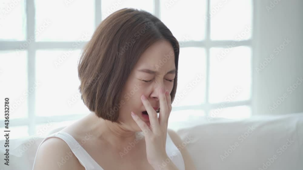 lazy asian woman face yawning using mobile smart phone on sofa couch at home. female in white living room yawn on day time need rest. tired and exhausted from workload sleep fall asleep and nap.