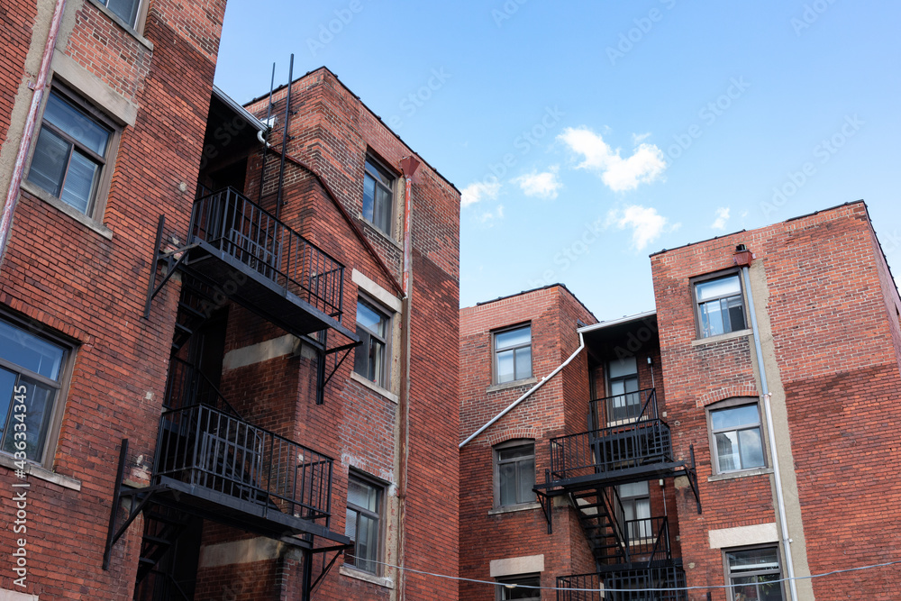 Naklejka premium Urban landscape rear view of old brick apartment buildings with black metal fire escapes against a bright blue sky, horizontal aspect