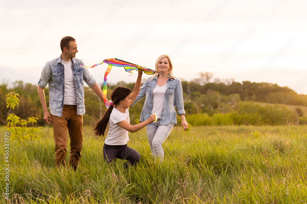Fototapeta premium Happy family in the park evening light. The lights of a sun. Mom, dad and baby happy walk at sunset. The concept of a happy family