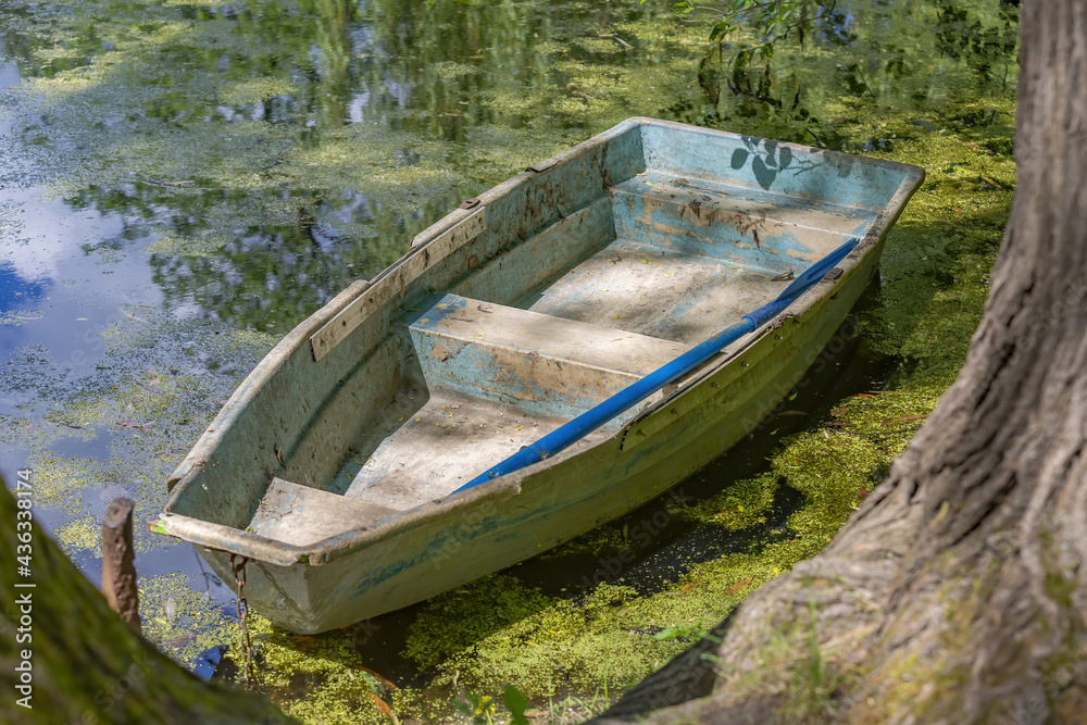 Old abandoned iron boat near a duckweed pond in the daytime