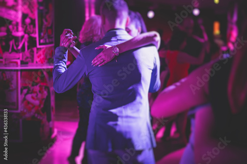 Couples dancing traditional latin argentinian dance milonga in the ballroom  tango salsa bachata kizomba lesson in the red  purple and violet lights  dance festival
