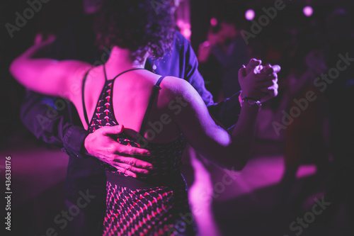 Couples dancing traditional latin argentinian dance milonga in the ballroom, tango salsa bachata kizomba lesson in the red, purple and violet lights, dance festival photo
