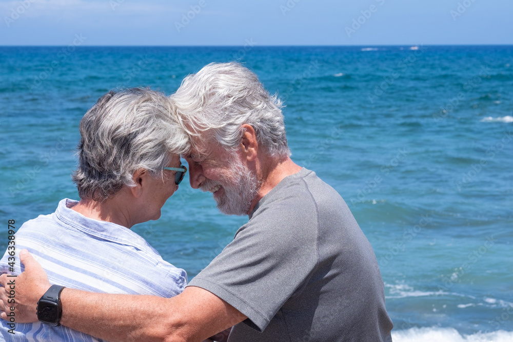 Back view of senior couple in love sitting on the beach looking each other. Two retired enjoying summer vacation and freedom