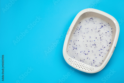 Cat litter tray with filler on light blue background, top view. Space for text