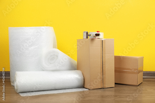 Bubble wrap rolls, tape dispenser and cardboard boxes on floor near yellow wall photo