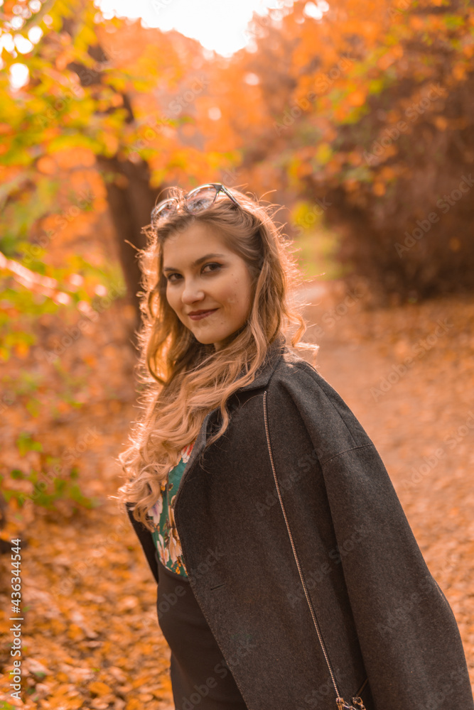 A joyful young girl in a black cloak stands in chameleon glasses in autumn. Yellow forest, green grass, blonde. looking at camera enjoy concept