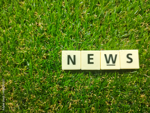 Selective focus.Scrabble letters with text NEWS on green grass background.