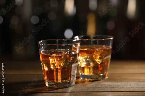 Fototapeta Naklejka Na Ścianę i Meble -  Glasses of whiskey with ice on wooden table in bar, space for text