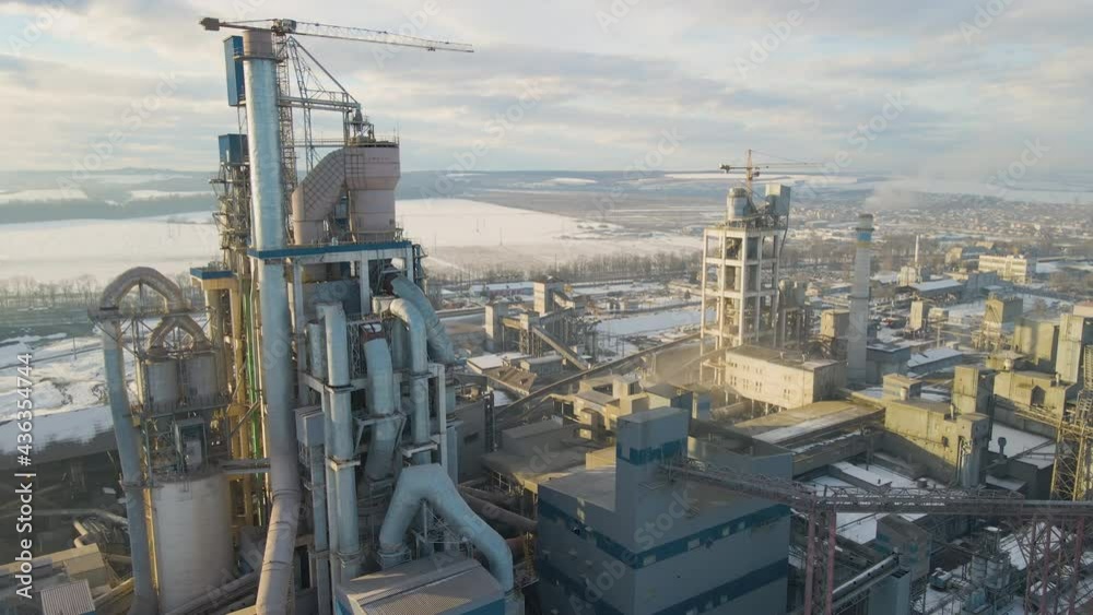 Aerial view of cement plant with high factory structure and tower crane at industrial production area at sunset.