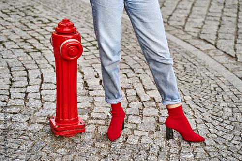 Woman legs in red knitted fabric block heel sock shoes and blue denim jeans pants near red street fire hydrant