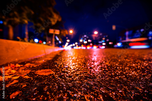 Rainy autumn night in the city  the glowing lights of approaching cars. View from the side of the road at the level of the asphalt