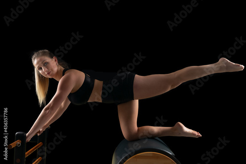 Woman doing pilates exercises in a reformer, black backgound, low key.