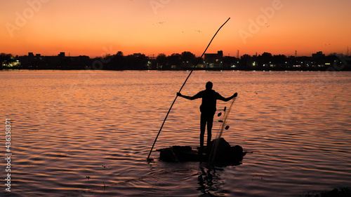 Fisherman on a small boat catching freshwater fish in nature river during sunset © Arnav Pratap Singh