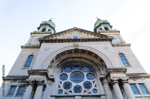 Straight on view of a gray stone church with verdigris copper cupolas, rose window, horizontal aspect