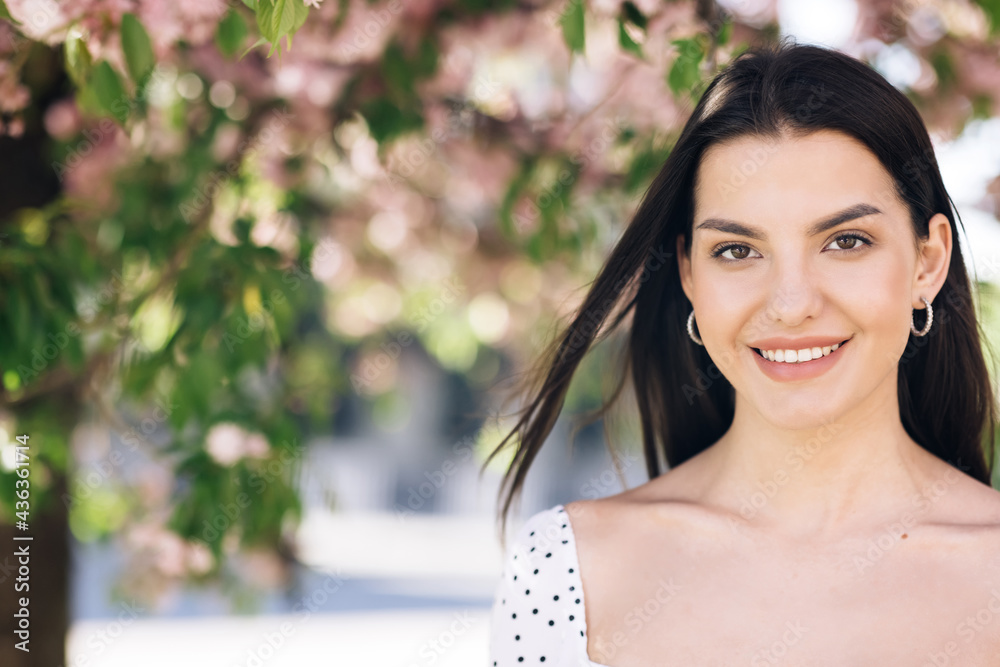 Beautiful smiling confident young ethnic woman pretty face looking at camera posing alone at park on a background of sakura trees. Happy millennial ethnicity girl student professional front portrait. Beautiful smiling confident young ethnic woman pretty face looking at camera posing alone at park on a background of sakura trees. Happy millennial ethnicity girl student professional front portrait.
