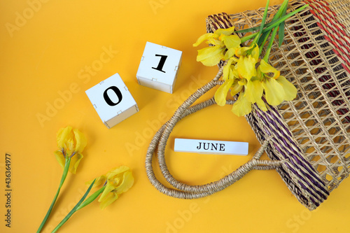 Calendar for June 1: cubes with the numbers 0 and 1, the name of the month of June in English, yellow irises with a wicker basket on a yellow background, top view photo