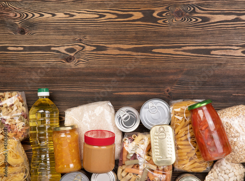 Food donations such as pasta, rice, oil, peanut butter, canned food, jam and other on brown wooden table, top view with copy space