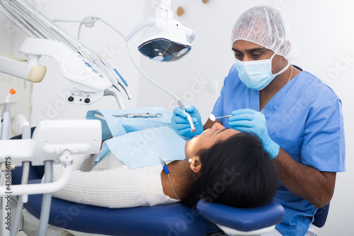 Portrait of focused hispanic dentist with woman patient during oral checkup in specialized dental office
