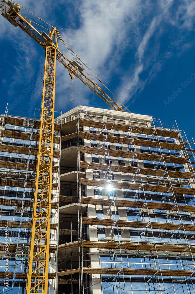 Modern construction finishing the facade of the house with glass window panels, scaffolding crane