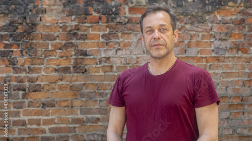 Portrait of a serious elderly man with a strong build of 45-50 years old in a T-shirt on the background of a brick wall. Maybe he's an actor or a construction worker.