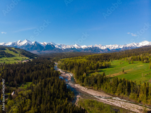 Top view of the beautiful green meadows and the Białka River, in the distance the snow-capped peaks of the Tatra Mountains. View from the air. View from the drone.