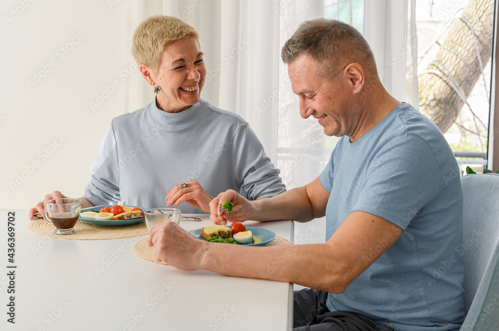 Seniors couple family have a breakfast at home, eating healthy food. Smiling and lauging, sitting at dinner table and have a great time together