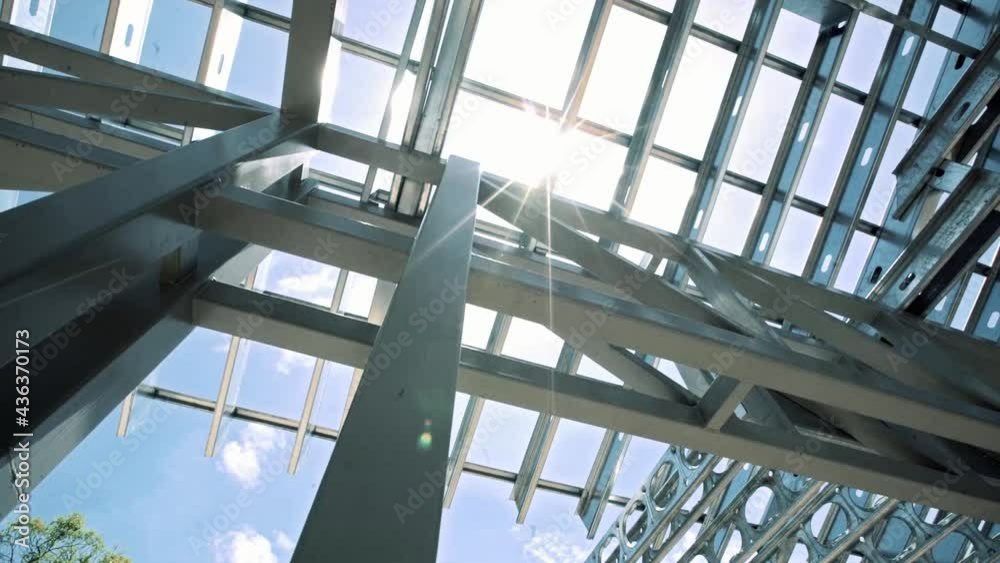 Bright sun shining through steel metallic building framing structure, low angle perspective on construction site with light flare.
