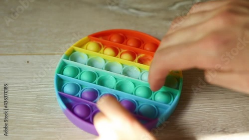 Child plays with touch anti-stress silicone pop it toy. Fingers press on rainbow soft bubbles and buttons. Trending game for development of fine motor skills and stress relief in children and adults photo