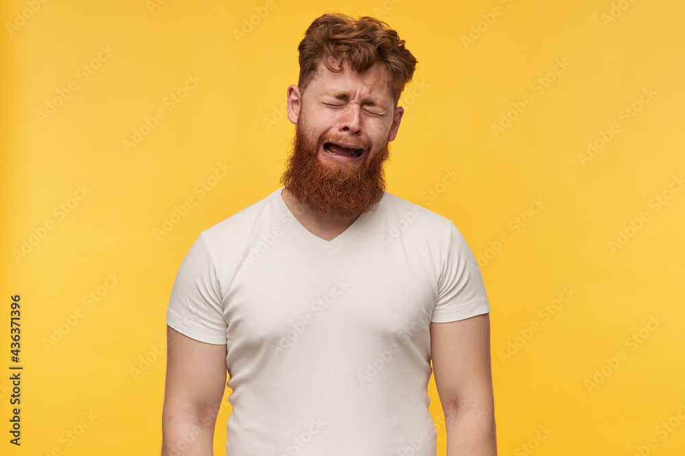 portrait of young man with big beard and red hair, wears blank t-shirt, feels depressed and tired, crying like a little boy. isolated over yellow background. portrait of young man with big beard and red hair, wears blank t-shirt, feels depressed and tired, crying like a little boy. isolated over yellow background.