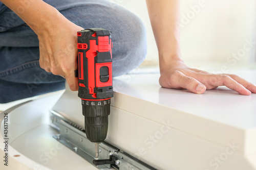 man assembling white table furniture at home using cordless screwdriver
