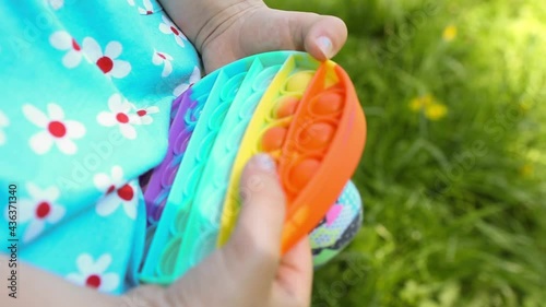 Girl plays with touch anti-stress silicone pop it toy outdoor in the garden. Fingers press on rainbow soft bubbles and buttons. Trending game for development of fine motor skills and stress relief photo