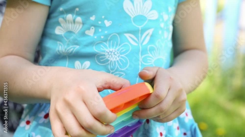 Girl plays with touch anti-stress silicone pop it toy outdoor in the garden. Fingers press on rainbow soft bubbles and buttons. Trending game for development of fine motor skills and stress relief