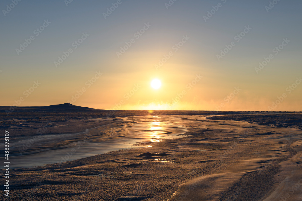 Arctic landscape in winter time. Small river with ice in tundra. Sunset.