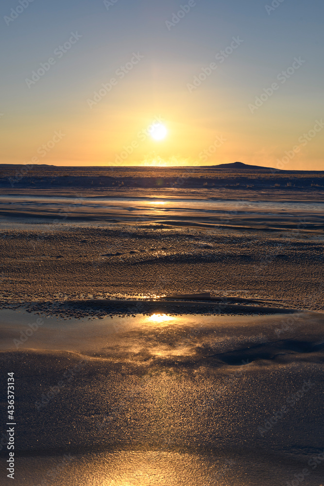 Arctic landscape in winter time. Small river with ice in tundra. Sunset.