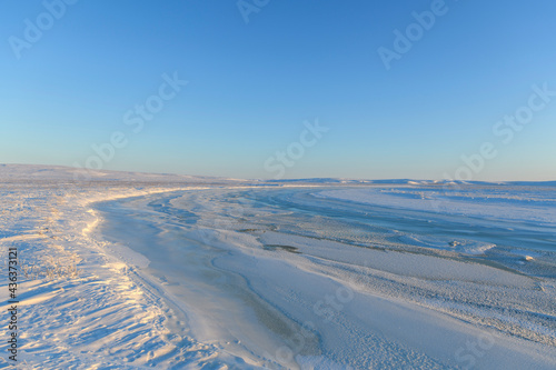 Arctic landscape in winter time. Small river with ice in tundra. Sunset.