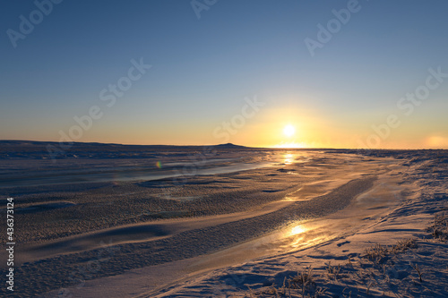 Arctic landscape in winter time. Small river with ice in tundra. Sunset.