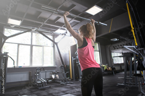 Rear view shot of unrecognizable female athlete lifting barbell, doing push press exercise