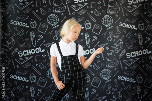 interesting smiling little girl in school clothes against a school board with drawings on the theme of School.  School concept. Back to school. © Olena Svechkova