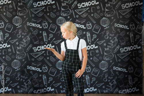 interesting smiling little girl in school clothes against a school board with drawings on the theme of School.  School concept. Back to school. © Olena Svechkova